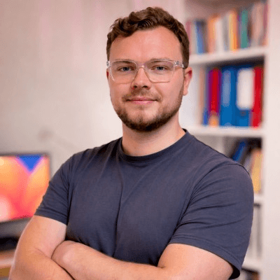 Тим Фойгт, руководитель консалтинга и развития бизнеса NETUNITY GmbH, со скрещёнными руками у книжной полки