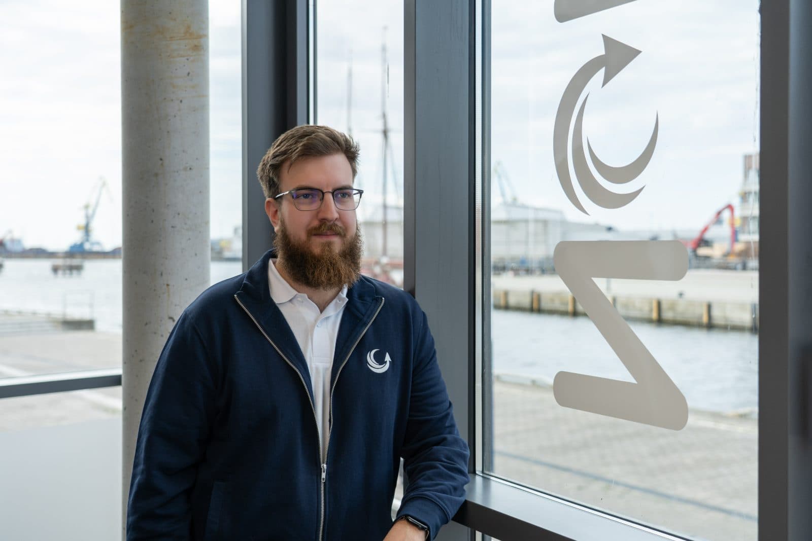 Simon Glowik am Fenster mit NordFlux-Logo und Blick auf den Hafen